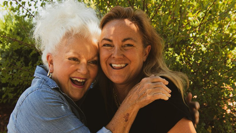 A woman wearing black blouse hugging an elderly mother in a denim shirt discussing a checklist for aging parents.t f