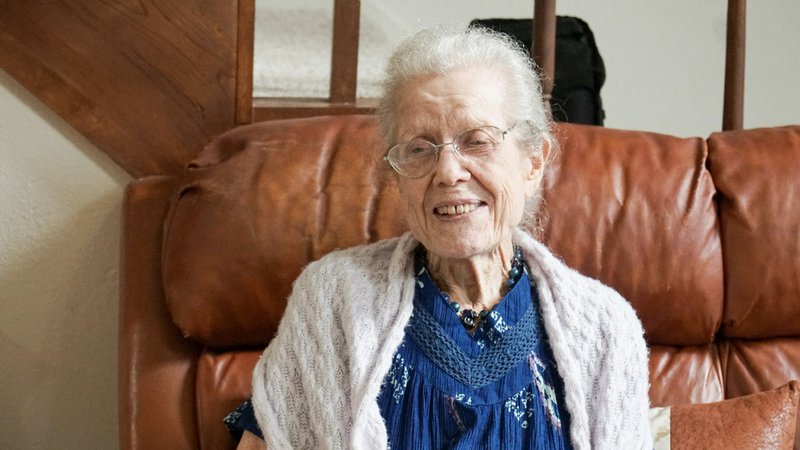woman in blue shirt and gray cardigan sitting on brown sofa displaying what is home care services.